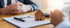 dos personas alrededor de una mesa con documentos, llaves y una casa de juguete encima