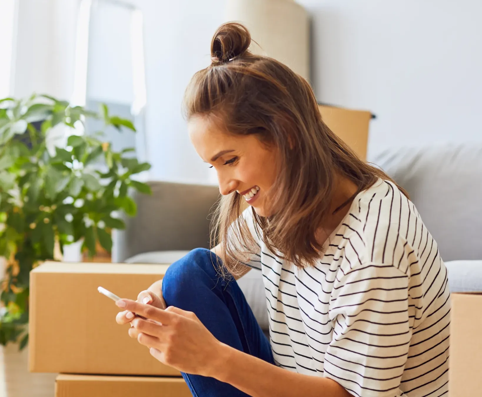 Beautiful young woman texting while moving to new apartment
